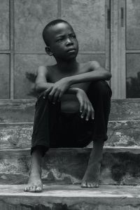 Grayscale Photo of Boy Sitting on Stair